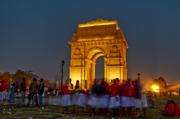India gate in delhi lit up in the dark with crowds of people below