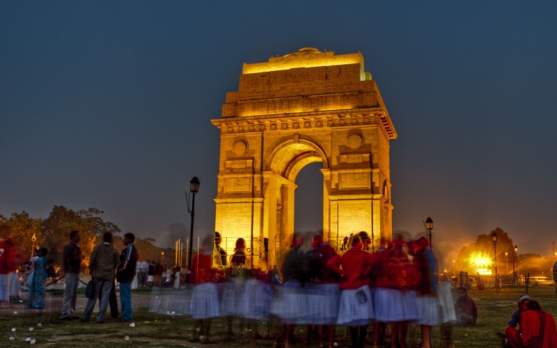 India gate in delhi lit up in the dark with crowds of people below